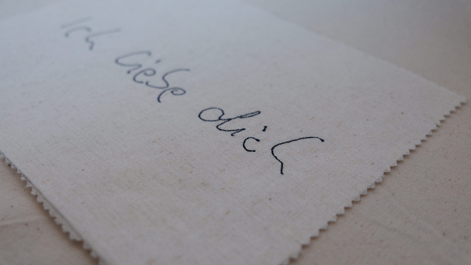 Die gestickte Notiz „Ich liebe dich“ ungerahmt auf naturfarbenem Leinen