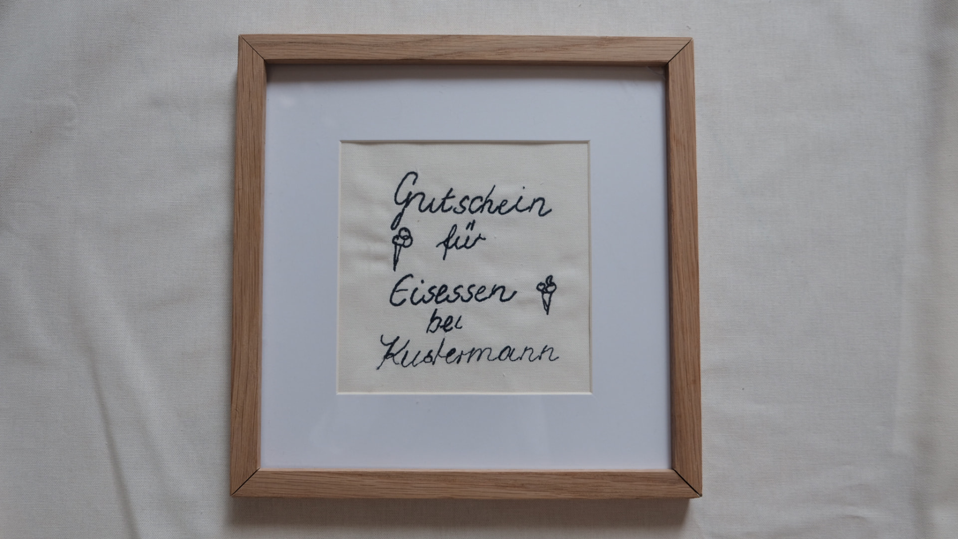 Gestickter Gutschein „Gutschein für Eisessen bei Kustermann“ in helle Eiche gerahmt